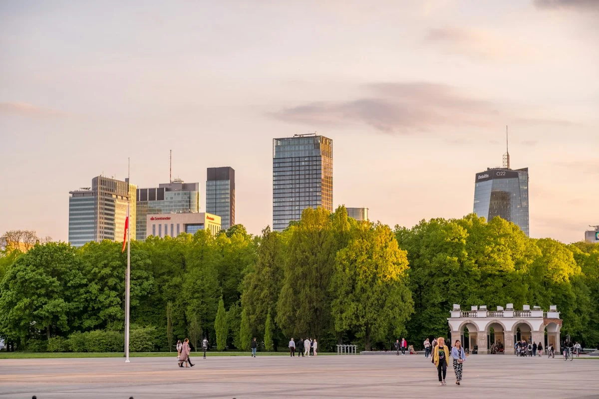Zielony park w centrum Warszawy, za drzewami wieżowce Śródmieścia