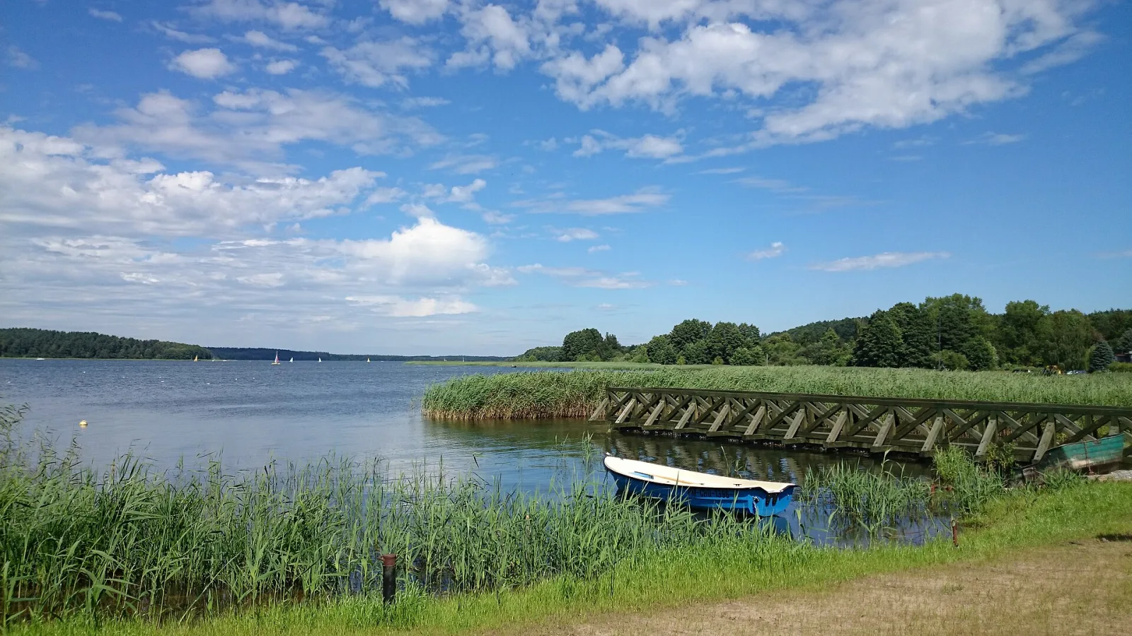 Lake Charzykowskie in Bory Tucholskie, seen from the shore with a jetty, a small boat and sailboats on the water