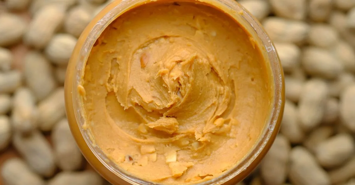 A jar of peanut butter surrounded by peanuts