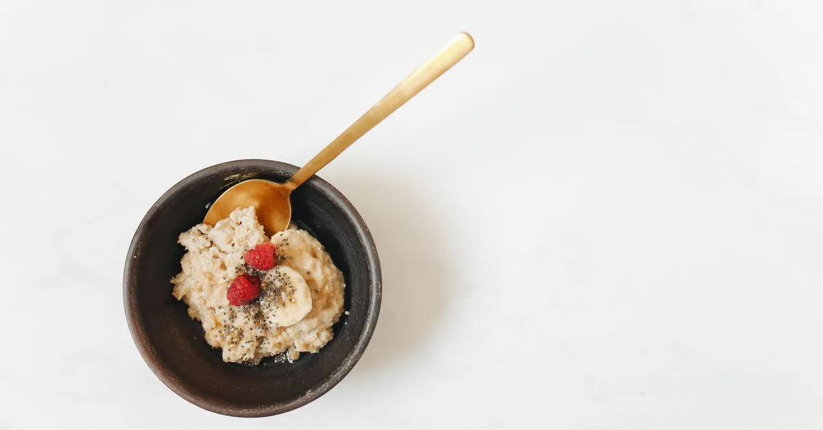 Bowl of cooked plain oatmeal next to a curious dog