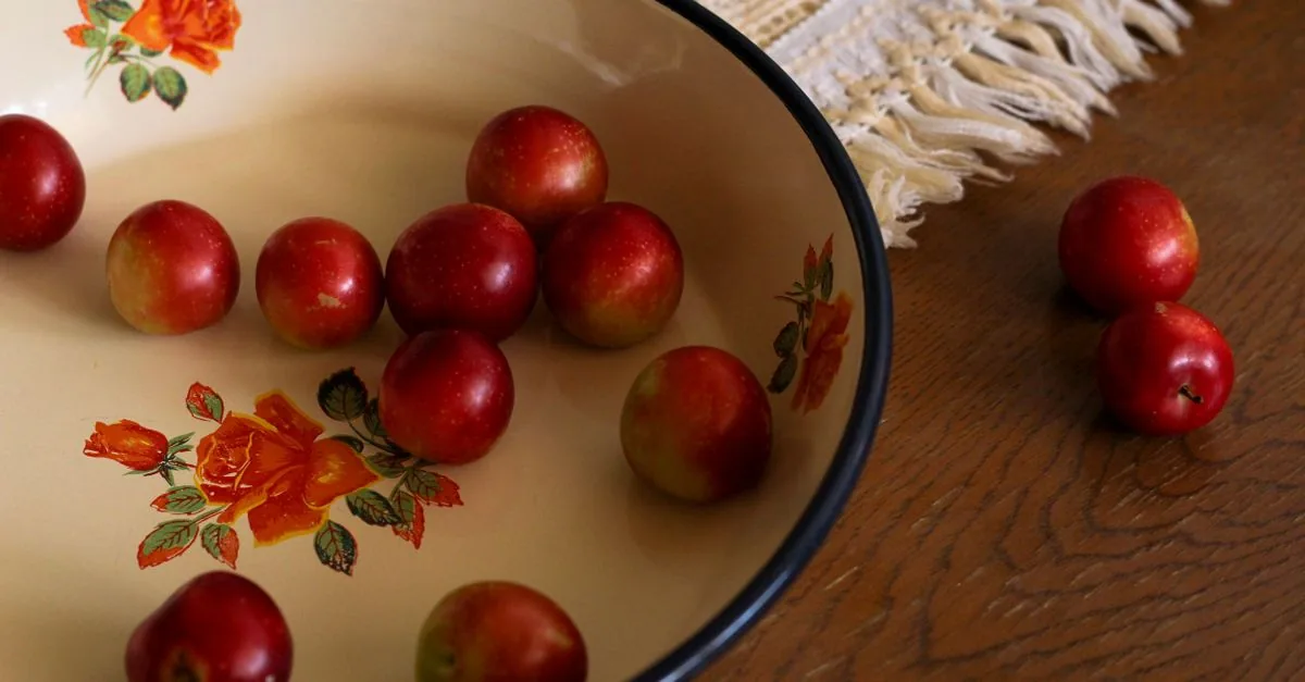 Dog sitting next to a bowl of fresh plums on a table